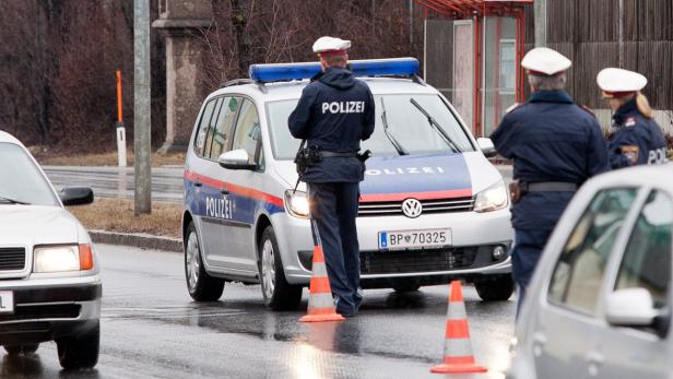 Ein Polizist steht neben einem Polizeiauto auf einer regnerischen Straße.