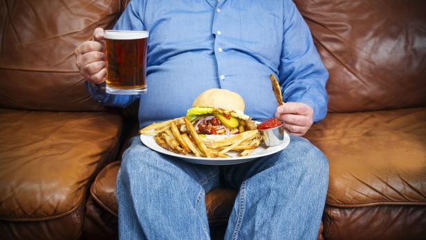 Overweight man over-eating on a couch