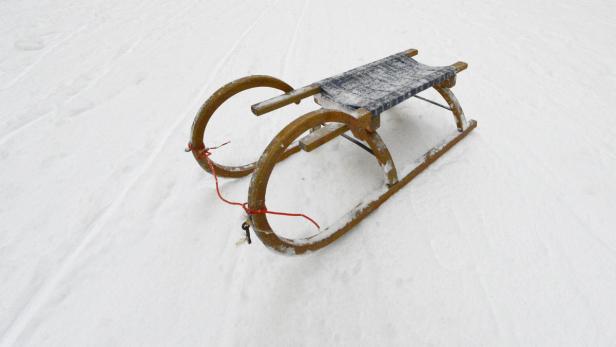 Ein Holzschlitten steht auf einer Schneefläche.