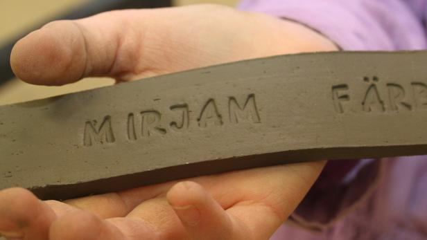 Eine Person hält einen Ziegelstein mit der Aufschrift „Mirjam Färber“.