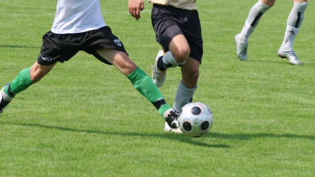 Fußballspieler dribbeln auf einem grünen Rasen mit einem Ball.