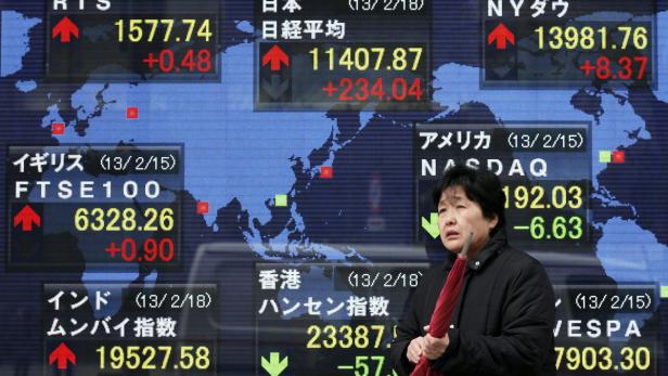 epa03589212 A pedestrian holds her umbrella in front of an electronic board showing the current figure of the Nikkei 225 Stock Average (top C) in Tokyo, Japan, 18 February 2013. Japanese stocks jumped 2.1 per cent as export-linked issues were bolstered by a weaker yen. The benchmark Nikkei 225 Stock Average gained 234.04 points, or 2.09 per cent, to end at 11,407.87 while the yen fell against major currencies after Japan&#039;s monetary easing policies were not directly criticized by financial leaders at the Group of 20 major economies over the weekend. EPA/KIYOSHI OTA
