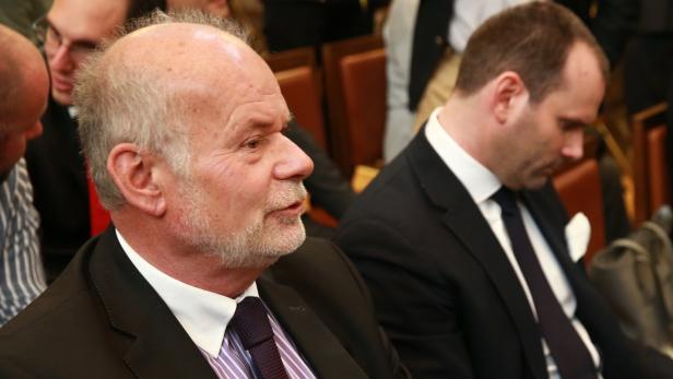 Zwei Männer in Anzügen sitzen während einer Veranstaltung.