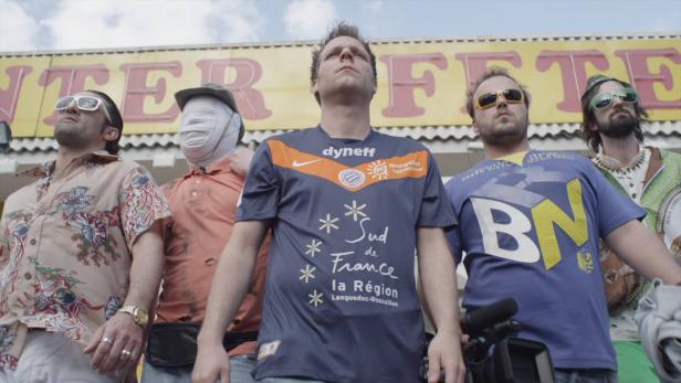 Fünf Männer stehen vor einem Gebäude mit der Aufschrift „Fete“.