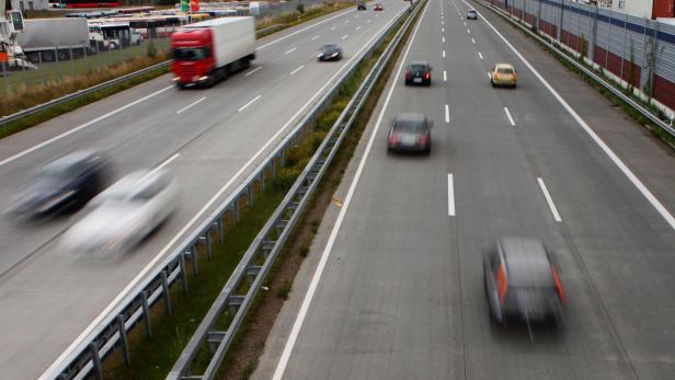 Mehrspurige Autobahn mit mehreren vorbeifahrenden Autos und einem Lkw, aufgenommen von einer Brücke.