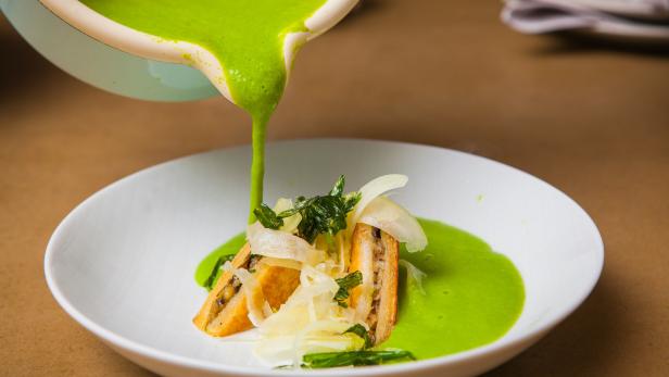 Grüne Soße wird über ein Gericht mit Brot und Gemüse gegossen.