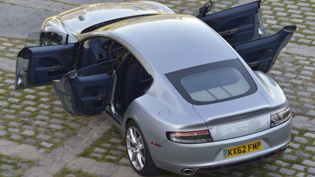 Ein silberner Aston Martin Rapide S mit geöffneten Türen steht auf einem Pflasterweg.