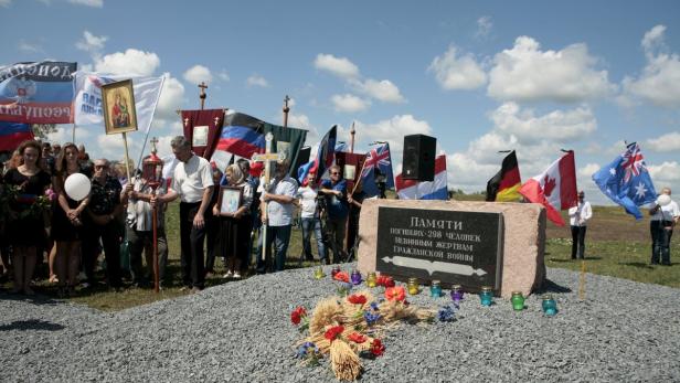 Eine Gruppe von Menschen steht vor einem Denkmal mit verschiedenen Flaggen, darunter die deutsche und die kanadische.