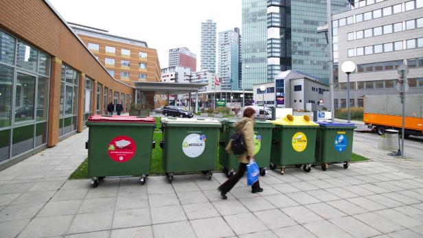 Eine Frau geht an einer Reihe von Müllcontainern zur Mülltrennung vorbei.