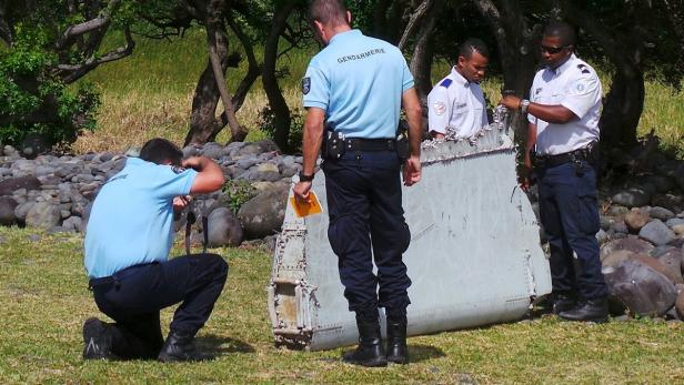 Französische Gendarmen untersuchen ein Trümmerteil auf einer Wiese.