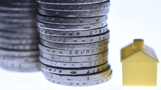 Ein Stapel von 2-Euro-Münzen neben einem kleinen gelben Spielzeughaus.