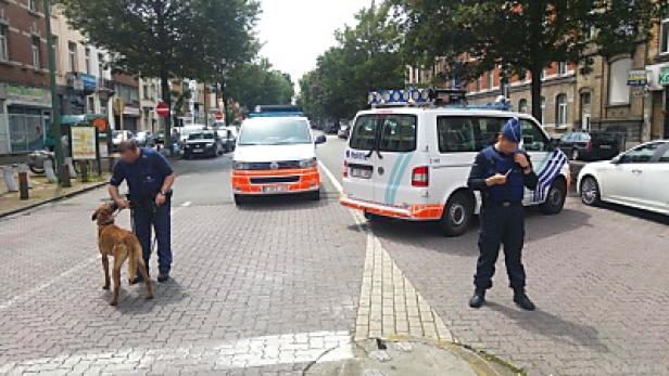 Zwei Polizisten und zwei Polizeiwagen stehen auf einer Straße.