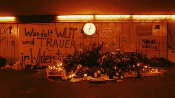 Eine Gedenkstätte mit Blumen, Kerzen und Graffiti-Botschaften wie „Wandelt Wut und Trauer in Widerstand“.