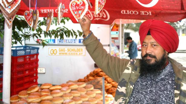 Ein Mann mit Turban verkauft Krapfen auf einem Marktstand mit Lebkuchenherzen.