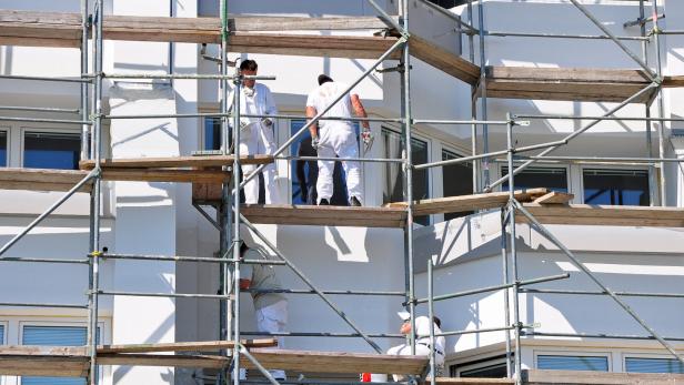 Mehrere Bauarbeiter arbeiten auf einem Gerüst an der Fassade eines Gebäudes.
