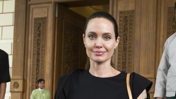Angelina Jolie in einem schwarzen Kleid vor einem verzierten Holzhintergrund.