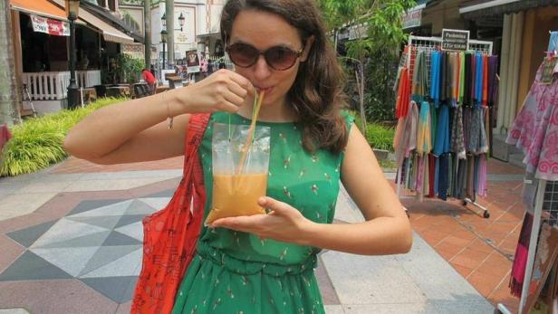 Eine Frau trinkt ein Getränk aus einer Plastiktüte mit einem Strohhalm auf einer belebten Straße.