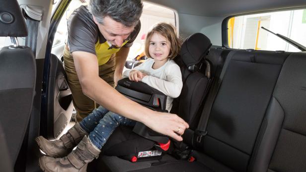 Ein Mann befestigt ein kleines Mädchen in einem Kindersitz im Auto.