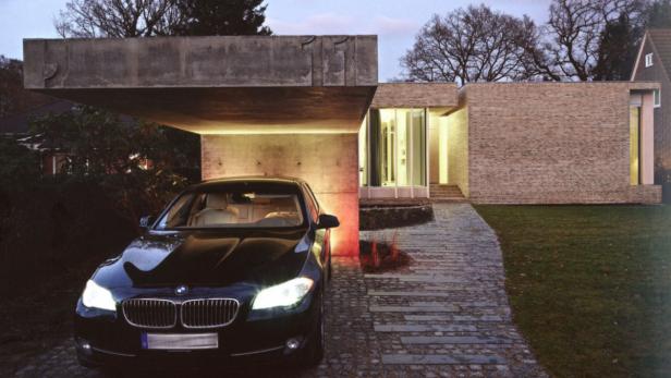 Ein schwarzer BMW parkt vor einem modernen Haus mit Carport.