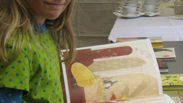 Ein junges Mädchen liest ein Bilderbuch an einem Tisch.