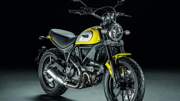 Eine gelbe Ducati Scrambler Desert Sled steht vor einem schwarzen Hintergrund.