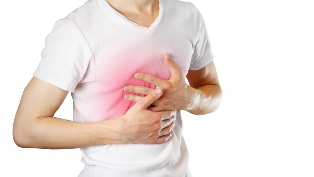 A man holds the Breasts. The pain in his chest. Heartburn. Stomach hurts. Sore point highlighted in red. Closeup. Isolated on white