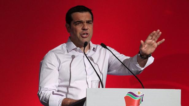 Alexis Tsipras hält eine Rede vor einem roten Hintergrund.