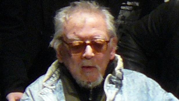 Ein älterer Mann mit Brille und Bart blickt in die Kamera.