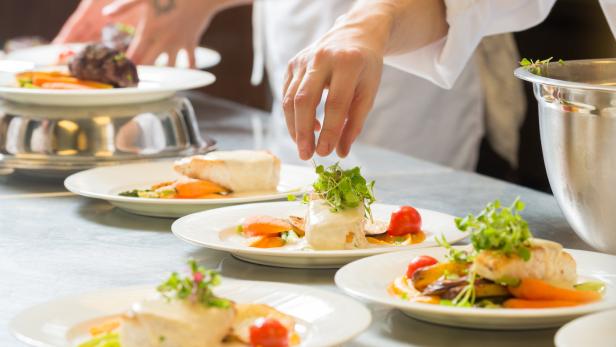 Ein Koch garniert Teller mit Fisch, Gemüse und Soße.