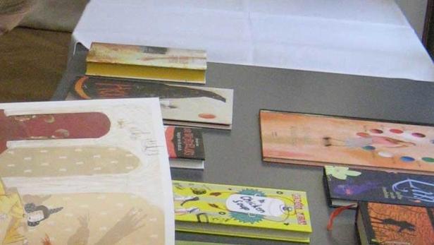 Ein Mädchen liest ein Bilderbuch; weitere Bücher liegen auf einem Tisch.