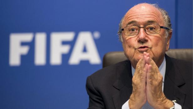 Sepp Blatter sitzt vor einem FIFA-Logo und hält die Hände gefaltet.