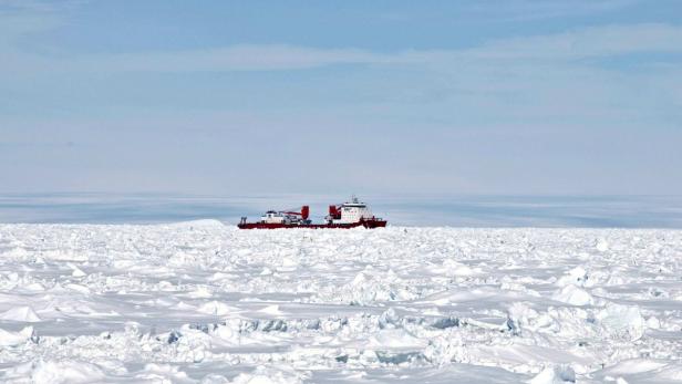 Ein rot-weißes Schiff fährt durch eine eisige Landschaft.
