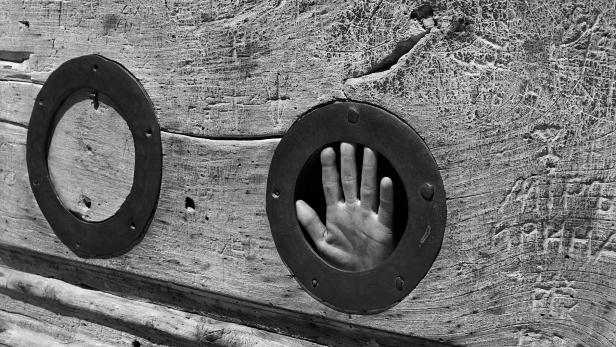 Eine Hand ragt durch ein Loch in einem alten Holzblock.