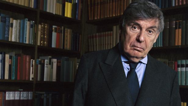 Ein Mann in Anzug und Krawatte steht vor einem Bücherregal.