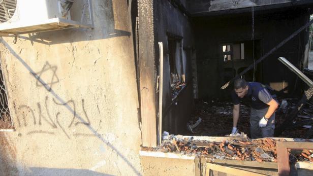 Ein Ermittler untersucht die Ruine eines ausgebrannten Hauses, an dessen Wand ein Davidstern zu sehen ist.