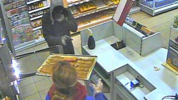 Ein maskierter Mann bedroht eine Kassiererin mit einer Waffe in einem Geschäft.