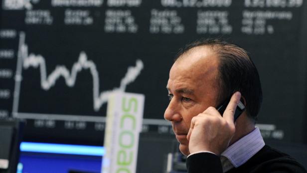 Ein Mann telefoniert vor einer Anzeigetafel mit Börseninformationen.