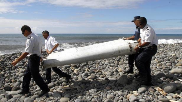 Polizeibeamte tragen ein Trümmerteil am Strand.