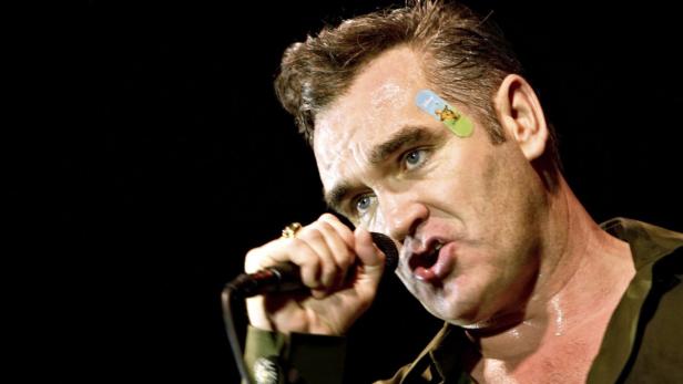 Morrissey singt mit einem Pflaster auf der Stirn in ein Mikrofon.