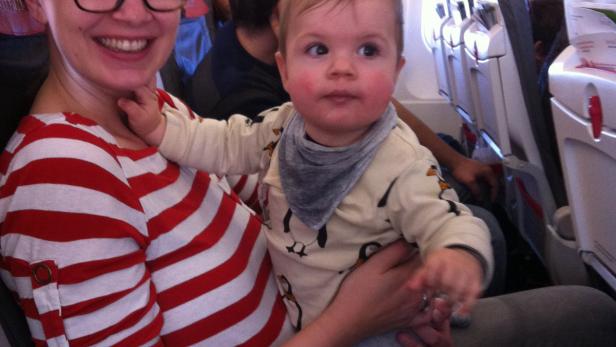 Eine Frau mit Brille hält ein Baby im Arm in einem Flugzeug.