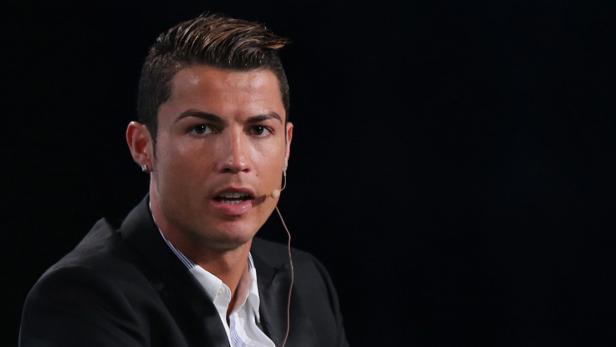 Cristiano Ronaldo trägt ein schwarzes Sakko und ein Headset-Mikrofon.