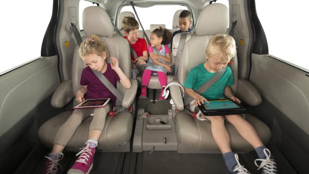 Fünf Kinder sitzen angeschnallt in einem Auto, zwei davon spielen mit Tablets.