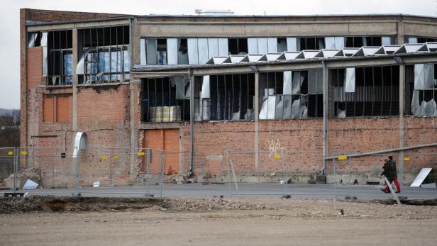 Ein verlassenes Backsteingebäude mit zerbrochenen Fenstern und Bauzäunen davor.