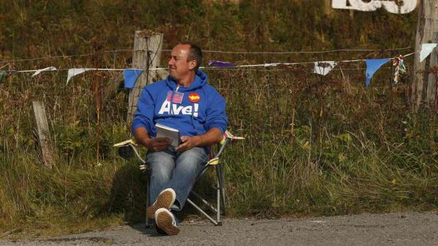 Ein Mann sitzt auf einem Campingstuhl und liest ein Buch.