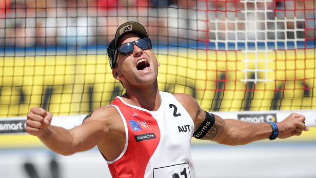 Ein Beachvolleyballspieler jubelt mit geballten Fäusten vor einem Netz.
