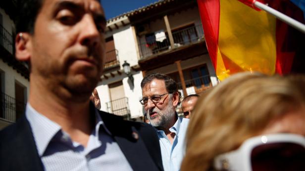 Mariano Rajoy spricht mit Menschen vor einem Gebäude mit einer spanischen Flagge.