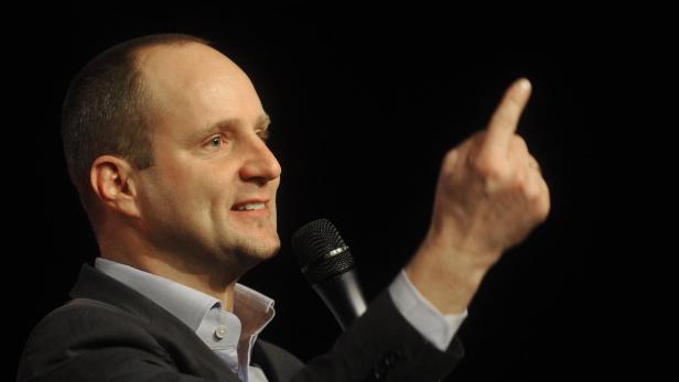 Ein Mann spricht in ein Mikrofon und hebt seinen Zeigefinger.