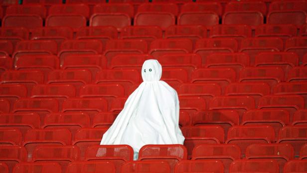 Eine Person in einem weißen Laken sitzt auf einem roten Sitzplatz in einem Stadion.