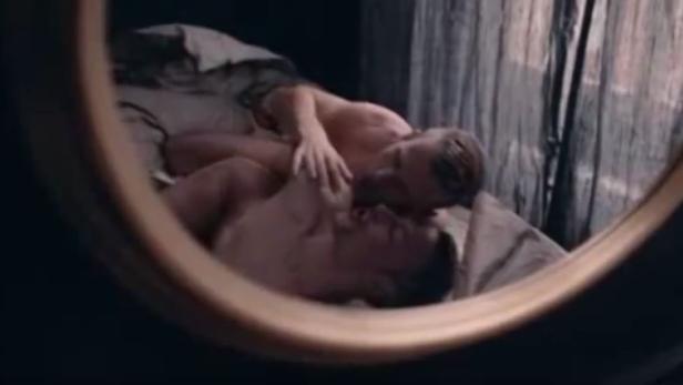 Zwei Männer liegen in einem Bett, gesehen durch einen Spiegel.