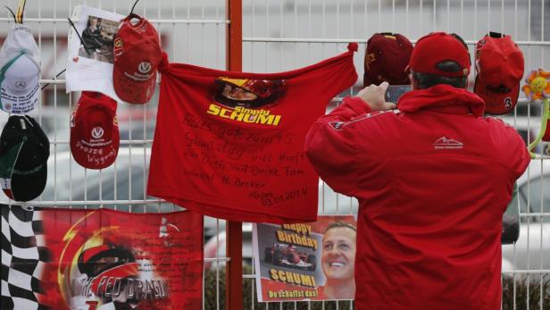 Ein Mann fotografiert eine Gedenkstätte für Michael Schumacher mit T-Shirts, Kappen und Botschaften.